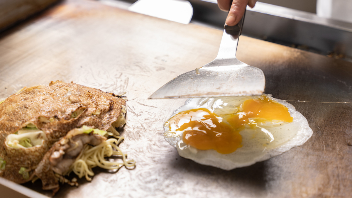 ライブキッチンの鉄板で広島風お好み焼きに入れる卵を焼いている様子