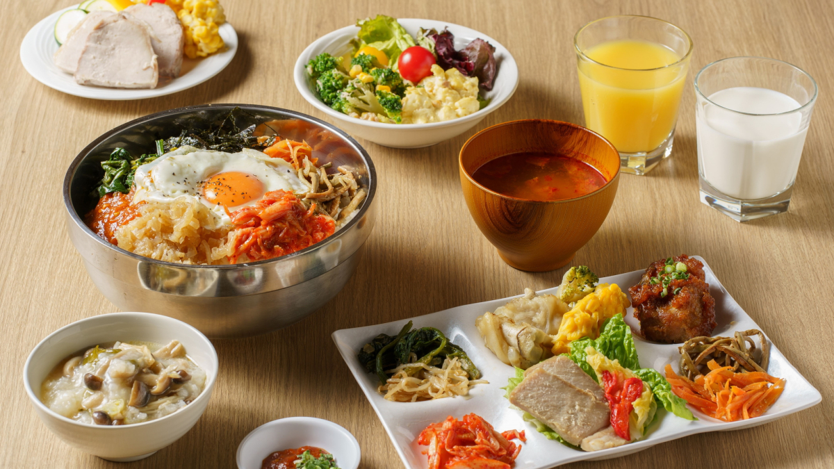 ビビンバ、各種ナムル、野菜サラダ、スープ、オレンジジュース等が並んだ韓国風朝食ビュッフェの写真