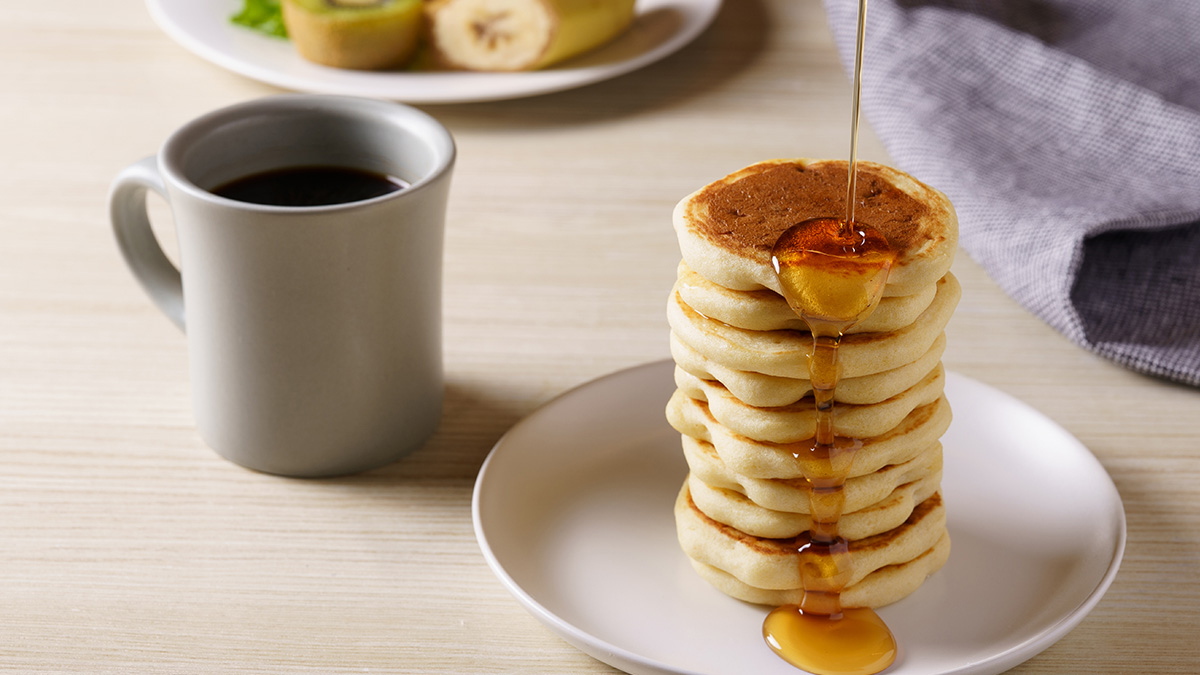 Pouring maple syrup over stacked pancakes