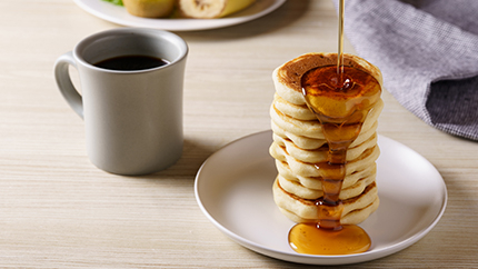 Pouring maple syrup over stacked pancakes